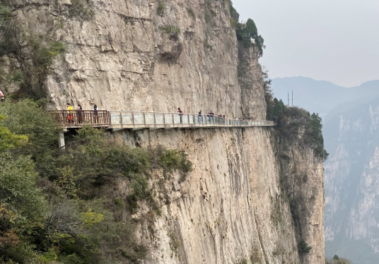 people walking over a bridge on the side of a cliff